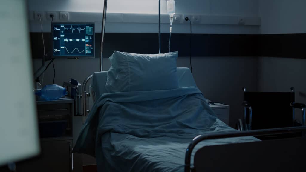 Empty hospital bed with monitoring equipment and IV stand in a patient room
