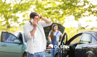 A distressed man standing between two damaged cars and a woman