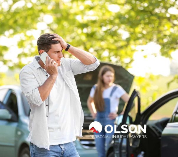A distressed man standing between two damaged cars and a woman