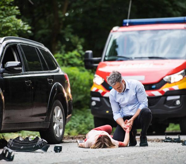 A man helping a young woman lying unconscious after a car accident