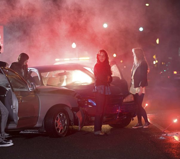 A group of people gathered around a car at a foggy nighttime roadside