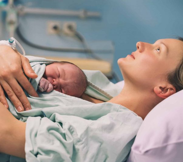 Mother and newborn. Child birth in maternity hospital. Young mom hugging her newborn baby after delivery. Woman giving birth. First moments of baby life after labor.