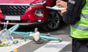 Policeman writes a ticket standing in front of a red car that hit a cyclist on a pedestrian lane