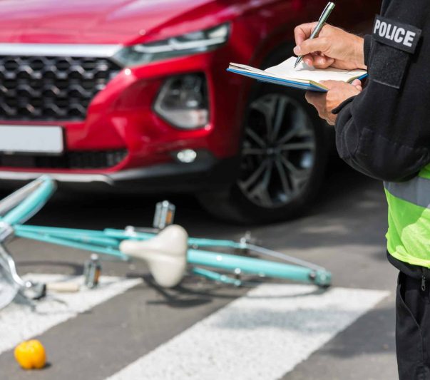 Policeman writes a ticket standing in front of a red car that hit a cyclist on a pedestrian lane