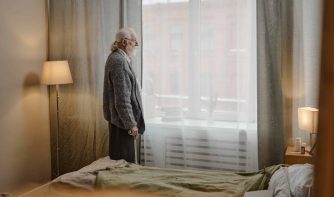 older man standing by window contemplating