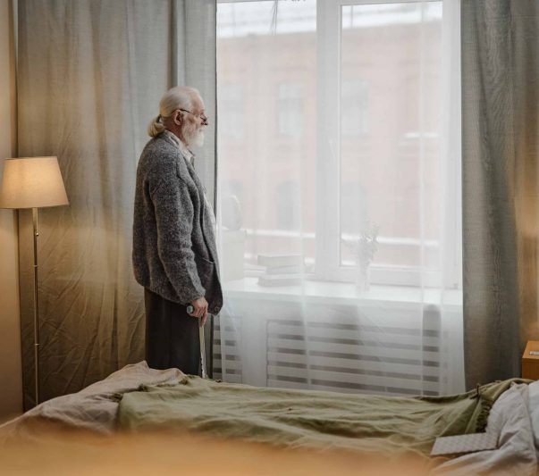 older man standing by window contemplating